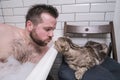 Man bathes in a bath in lush foam, next to him lies his adored cat, which is very interested in what is happening. Royalty Free Stock Photo