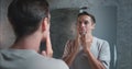 Man in bathroom looking at mirror applies moisturiser for face importance moisturise face for skin health. Moisturize