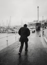 A man battles against wind and rain alongside Ramsgate Royal Harbour on a cold winter day. In monochrome