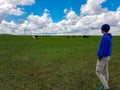 A man in a beanie observing a heard of horses grazing on a vast pasture in Xilinhot, Inner Mongolia. A few wind turbines Royalty Free Stock Photo