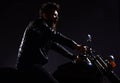 Man with beard, biker in leather jacket sitting on motor bike in darkness, black background. Macho, brutal biker in Royalty Free Stock Photo