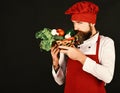 Man with beard on black background, copy space. Vegetarian diet concept. Cook with tricky face in burgundy uniform