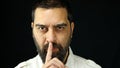Man with beard on black background holding index finger in front of mouth making silence sign. Royalty Free Stock Photo