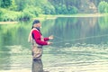 A man with a beard in a bondana and in marsh boots fishing on the river