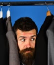 Man with beard by clothes rack. Designer hides among suits