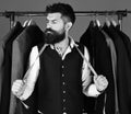 Man with beard by clothes rack. Tailor with serious face and measuring tape near custom jackets