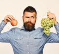 Man with beard holds bunch of green grapes and apple isolated on white background. Winegrower with tricky face holds