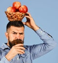 Man with beard holds wicker bowl of fruit and juice on blue background. Farmer with busy face drinks apple juice and