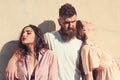 Man with beard hugs two ladies on hot sunny day. Threesome suffers of heat on summer day, wall on background. Girls Royalty Free Stock Photo