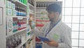 A man with a beard in a lab coat holds a medicine bottle while using a tablet in a modern pharmacy interior Royalty Free Stock Photo