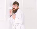 Man with beard and mustache eavesdrops using cup near wall. Hipster in bathrobe on surprised face secretly listen Royalty Free Stock Photo