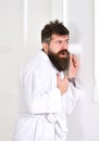 Man with beard and mustache eavesdrops using mug near wall. Hipster in bathrobe on concentrated face secretly listen Royalty Free Stock Photo