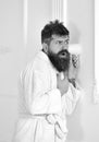 Man with beard and mustache eavesdrops using mug near wall. Hipster in bathrobe on concentrated face secretly listen Royalty Free Stock Photo