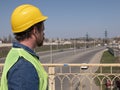 A man with a beard and mustache in a helmet is standing on the bridge against the backdrop of the highway.road service worker Royalty Free Stock Photo