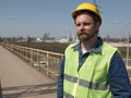 A man with a beard and mustache in a helmet is standing on the bridge against the backdrop of the highway.road service worker Royalty Free Stock Photo