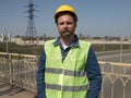 A man with a beard and mustache in a helmet is standing on the bridge against the backdrop of the highway.road service worker Royalty Free Stock Photo