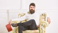 Man with beard and mustache sits on armchair, holds book, white wall background. Connoisseur on thoughtful face finished Royalty Free Stock Photo