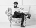 Man with beard and mustache sits on armchair, holds book, white wall background. Connoisseur on thoughtful face finished Royalty Free Stock Photo