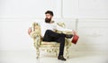 Man with beard and mustache sits on armchair, holds book, white wall background. Reflections on literature concept. Guy Royalty Free Stock Photo