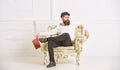 Man with beard and mustache sits on armchair, holds book, white wall background. Reflections on literature concept. Guy Royalty Free Stock Photo