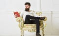 Man with beard and mustache sits on armchair and reading, white wall background. Connoisseur of literature concept