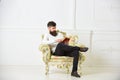 Man with beard and mustache sits on armchair and reading, white wall background. Connoisseur of literature concept Royalty Free Stock Photo