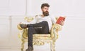 Man with beard and mustache sits on armchair and reading, white wall background. Connoisseur of literature concept