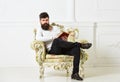 Man with beard and mustache sits on armchair and reading, white wall background. Connoisseur, professor enjoy literature