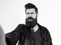 Man with beard and mustache on strict face looking at camera. Macho wears leather jacket, white background. Hipster Royalty Free Stock Photo