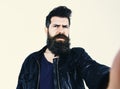 Man with beard and mustache on strict face looking at camera. Macho wears leather jacket, white background. Hipster Royalty Free Stock Photo