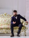Man with beard and mustache wearing fashionable classic suit, sits on old fashioned couch or sofa. Fashion and style