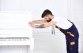 Man with beard and mustache, worker in overalls pushes piano, white background. Delivery service concept. Loader moves