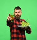 Man with beard presents glass of grape juice or white wine isolated on green background. Farming and gardening concept