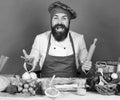 Man with beard sits by countertop on green background. Cook with excited face in burgundy uniform holds rolling pin Royalty Free Stock Photo