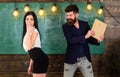Man with beard slapping student, chalkboard on background. Schoolmaster punishes student with slapping on her