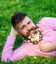 Man with beard on smiling face enjoy nature. Bearded man with daisy flowers lay on meadow, lean on hand, grass