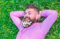 Man with beard on smiling face enjoy nature. Unite with nature concept. Bearded man with daisy flowers lay on grassplot Royalty Free Stock Photo