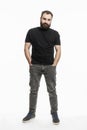 A man with a beard is standing with his hands in his pockets. Young man in jeans and a black T-shirt. Full height. White