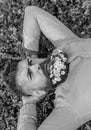 Man with beard on strict face enjoy nature. Bearded man with daisy flowers lay on grassplot, grass background