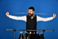 Man with beard takes measures by clothes rack with suits.
