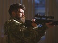 Man with beard wears camouflage clothing, dark interior background. Macho on suffering grimace face aiming at victim Royalty Free Stock Photo