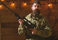 Man with beard wears camouflage clothing in wooden interior background. Gamekeeper concept. Hunter, brutal hipster with