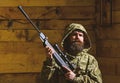 Man with beard wears camouflage hooded clothing, wooden interior background. Macho on strict face at gamekeepers house Royalty Free Stock Photo