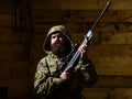 Man with beard wears camouflage hooded clothing, wooden interior background. Macho on strict face at gamekeepers house Royalty Free Stock Photo