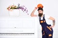 Man with beard, worker in overalls and helmet lean on piano, white background. Loader moves piano instrument. Delivery
