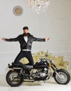 Man, bearded biker in leather jacket near motor bike in luxury living room interior background. Hipster biker brutal in Royalty Free Stock Photo