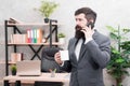 Man bearded businessman hold cup and smartphone. Coffee is pledge of successful negotiations. Caffeine addicted. Mobile