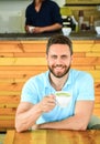 Man bearded guy drinks cappuccino at wooden table cafe. Cafe visitor happy face enjoy coffee caffeine drink. Caffeine