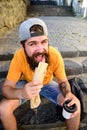 Man bearded hipster enjoy street food urban background. Hipster eat hot dog while sit on stairs outdoors. Urban food Royalty Free Stock Photo