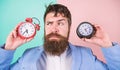 Man bearded hipster hold two different clocks. Guy unshaven puzzled face having problems with changing time. Changing